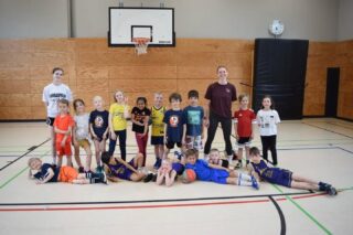 Saisonbericht u8  Der Jahrgang 2018 startete im September 2025 in seine erste Basketballsaison. Einige fieberten schon lange darauf hin, denn sie hatten bereits in der Ballbinis-Gruppe 3 Jahre zuvor bei uns angefangen und waren damals schon dem (in dem Alter noch) gelben Ball verfallen.
Wie viel die Kids in der Saison dazu gelernt haben und wie groß sie geworden sind, merke ich vor allem in der Retrospektive, wenn ich nun ein Jahr später einen neuen Jahrgang in der u8 willkommen heiße. Neben den individuellen Skills wie Korbleger, Dribbling und Passen, hat sich auch das Zusammenspiel stark entwickelt und zum Ende der Saison wurde von den meisten nicht nur einfach der Korb als Ziel gesehen, sondern auch Entscheidungen getroffen, wann es gut ist, den Ball zu passen, sowohl im Fastbreak, als auch im Halbfeld. 
Engagement und Einsatz auf dem Feld waren erfreulicherweise von Anfang an vorhanden, womit wir von Saisonbeginn an viele Teams vor allem in der Defense das Leben schwer machten. Im Laufe der Monate wurde unser "Turbo" immer besser und sowohl offensiv, als auch defensiv eingesetzt.
Ein zusätzliches Plus, über das sich jeder Coach freut, sind die engagierten Eltern, die ihre Kids zu allen Spielen fahren, weswegen wir niemals Probleme mit dem Kader hatten, und auch mal das Coaching bei einem Turnier wurfe übernommen, wenn ich wegen anderer Teams verhindert war.  Ich hoffe, alle hatten genau so viel Spaß wie ich, und bleiben uns noch lange erhalten. Und da ich nun mal Mädchencoach bin, hoffe ich ganz besonders die Mädels bald in einem meiner Team wiederzusehen.  Danke,
Eure Peti