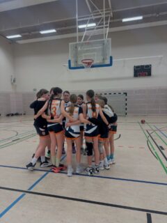 Saisonbericht wU14 II  Auch in dieser Saison entschieden wir uns wieder dafür, ein Team in der Bezirksliga zu melden und die Mädels aus der wU12 mitspielen zu lassen, um Erfahrungen zu sammeln.  Die Hinrunde begann mit einem knappen Sieg. In den nächsten Spielen zeigte sich jedoch, dass wir selten eine richtige Herausforderung hatten. Deshalb entschieden wir uns zur Rückrunde, in die Landesliga aufzusteigen, um uns weiterentwickeln zu können.  Dort wartete ein höheres Niveau auf uns. So mussten wir lernen, Niederlagen einzustecken, aber lernten, Verantwortung zu übernehmen, um jeden Rebound zu kämpfen, wie wichtig gute Defense ist, als Team zusammenzuhalten und den Kopf nicht hängen zu lassen.  Mindestens genauso wichtig wie das auf dem Feld ist aber das abseits des Feldes. Die Mädchen sind im Laufe der Saison zu einem echten Team zusammengewachsen. Sie haben sich gegenseitig unterstützt, sich füreinander gefreut und waren füreinander da, auch in Phasen, in denen es vielleicht nicht so gut lief.  Auch wenn wir die Saison nicht mit einem Sieg beenden konnten, nehmen wir viele schöne Momente mit, dass jede gezeigt hat, was in ihr steckt und sich weiterentwickelt hat.  Wir sind stolz auf euch und freuen uns darauf, euch weiterhin in den Hallen zu sehen.  Peti und Lili 
🧡💙  Für die wU14-2 spielten:
Alma, Alva, Ami, Annabell, Cleo, Cara, Emma, Elsa, Hannah, Hella, Helli, Helena, Jonna, Juno, Karla, Lorna, Lotti, Liv, Leni, Leo, Magda, Paule, Toni, Vicky und Zelda
